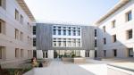 Modern courtyard between beige buildings with central glass atrium and small figures