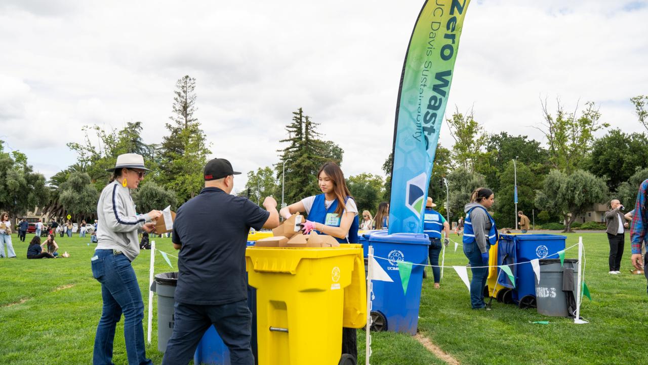 Volunteers at outdoor recycling station with large yellow bins and blue banner
