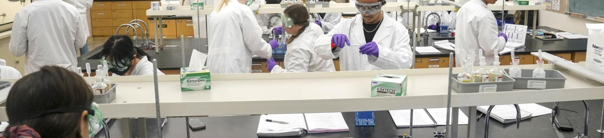 Group of students wearing lab coats in goggles in a lab